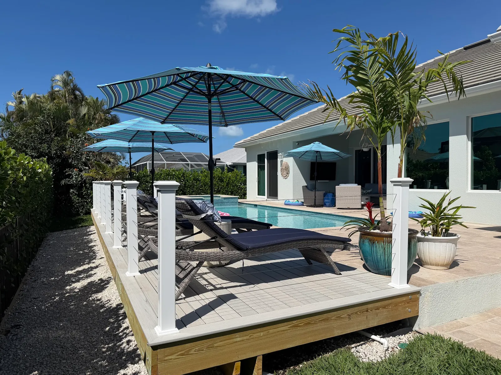 A composite pool deck with white posts, loungers and umbrellas, palms behind