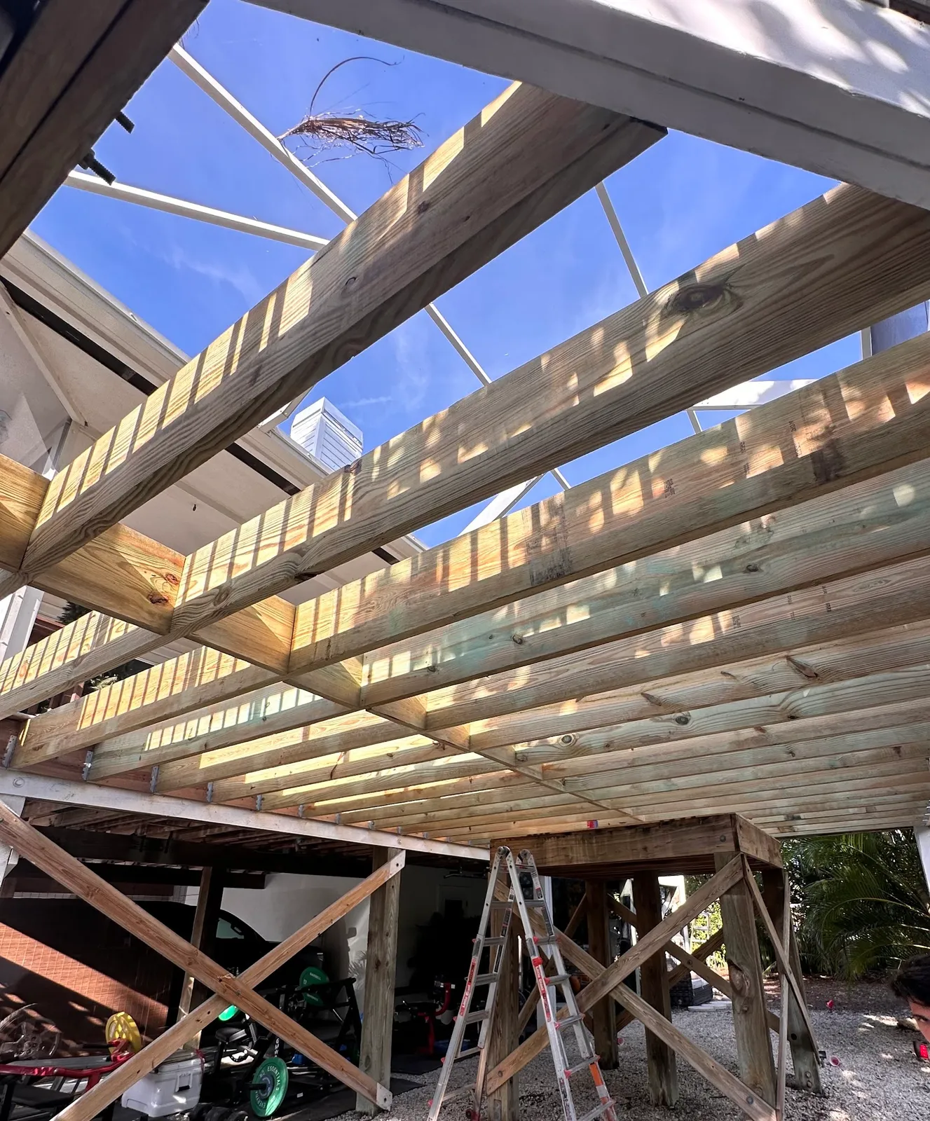 Pergola rafters seen from below during framing, against a blue sky